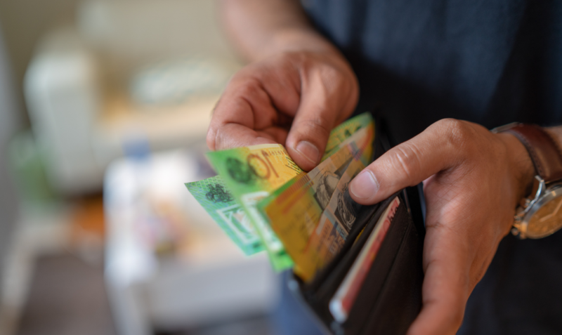 Close up of a person opening a wallet and holding $100 Australian bank notes.