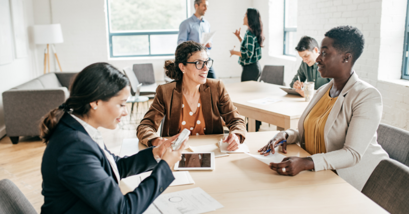 Three women in an office-like setting engaging in conversation.